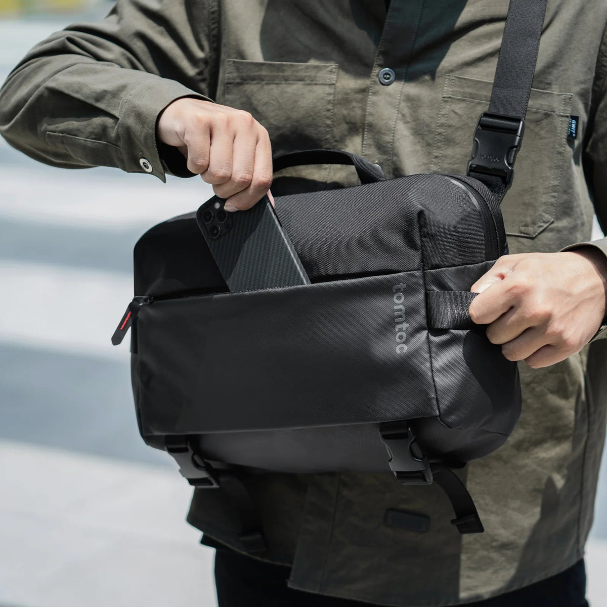 Person putting his phone into tomtoc T21L1D1 Business laptop sling bag with a blurred background