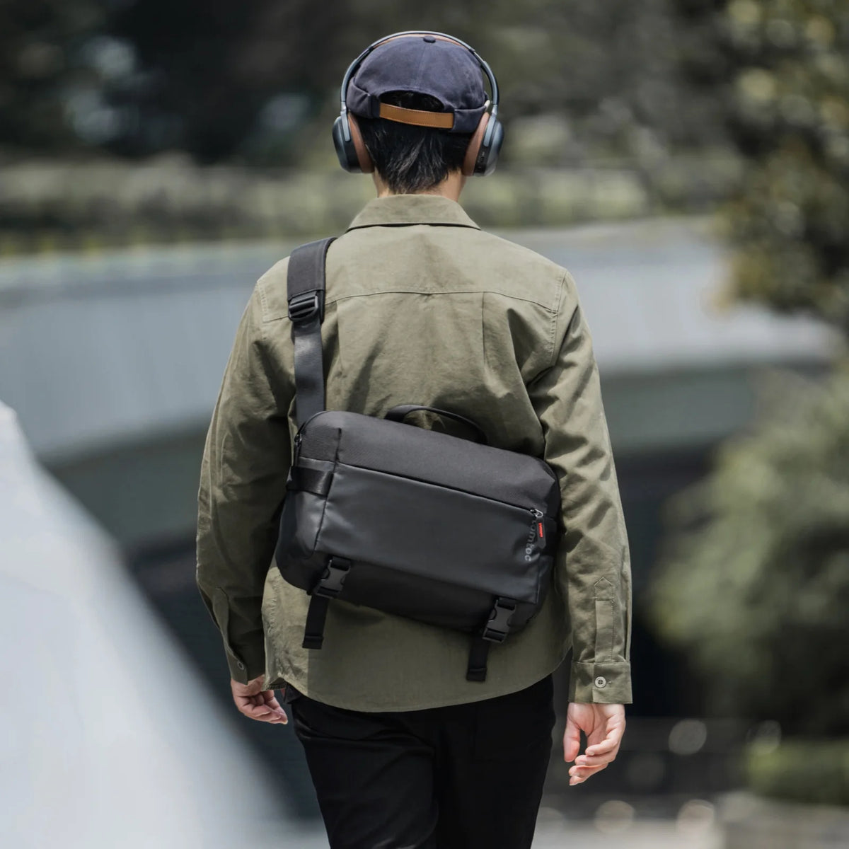 Person wearing a green jacket and tomtoc T21L1D1 Business laptop sling bag walking on urban street