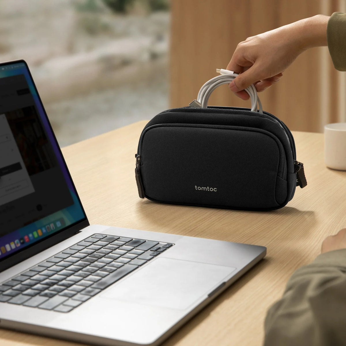 Person putting a cable into T12M1 black organiser pouch next to a laptop on a wooden table.