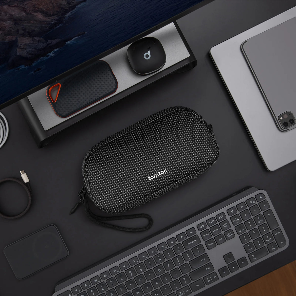 Black mesh pouch with 'tomtoc' branding on a desk with computer equipment.
